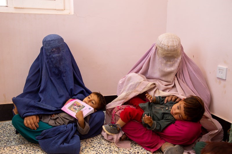To kvinner i burka sitter på gulvet med hvert sitt barn i fanget.