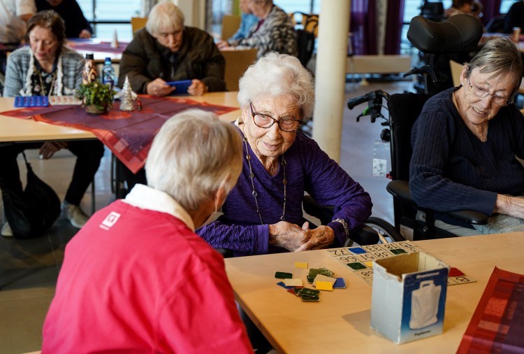 Mange eldre mennesker sitter rundt bord og spiller bingo.