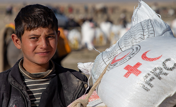 En ung gutt står ved siden av en sekk med ris ifra Røde Kors
