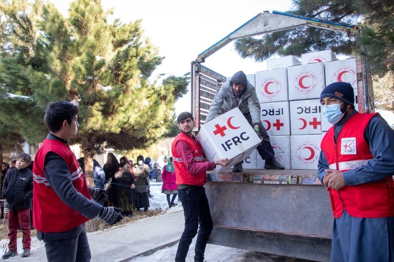 Fire menn løfter kasser med Røde Kors-logo på av en lastebil. 