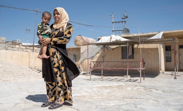 En kvinne står på et fabrikkområde med sin sønn på armen.