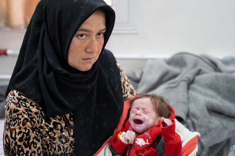 En kvinne sitter med en gråtende baby på fanget på et sykehus.
