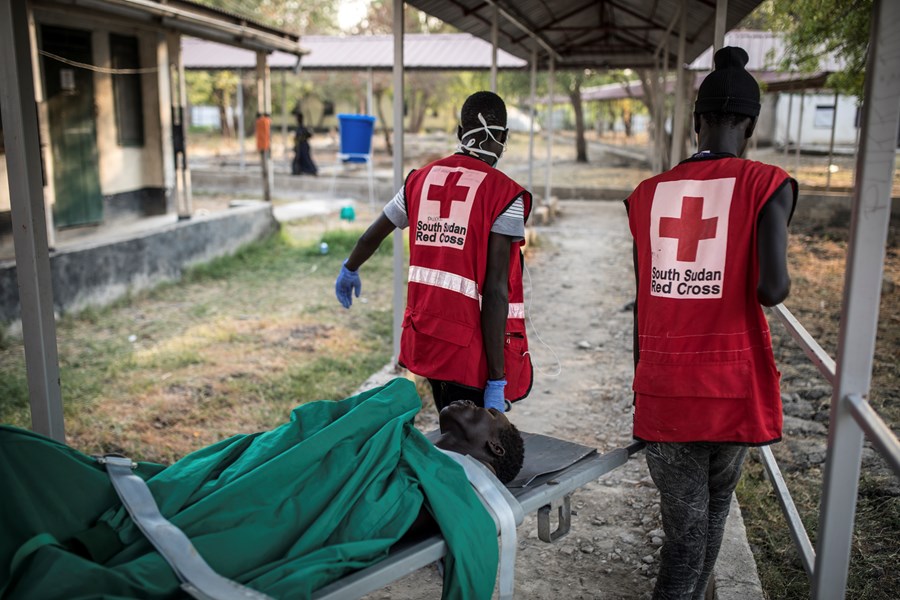 To frivillige fra Røde Kors bærer en båre med en person etter operasjon ved Røde Kors-sykehuset i Akobo.