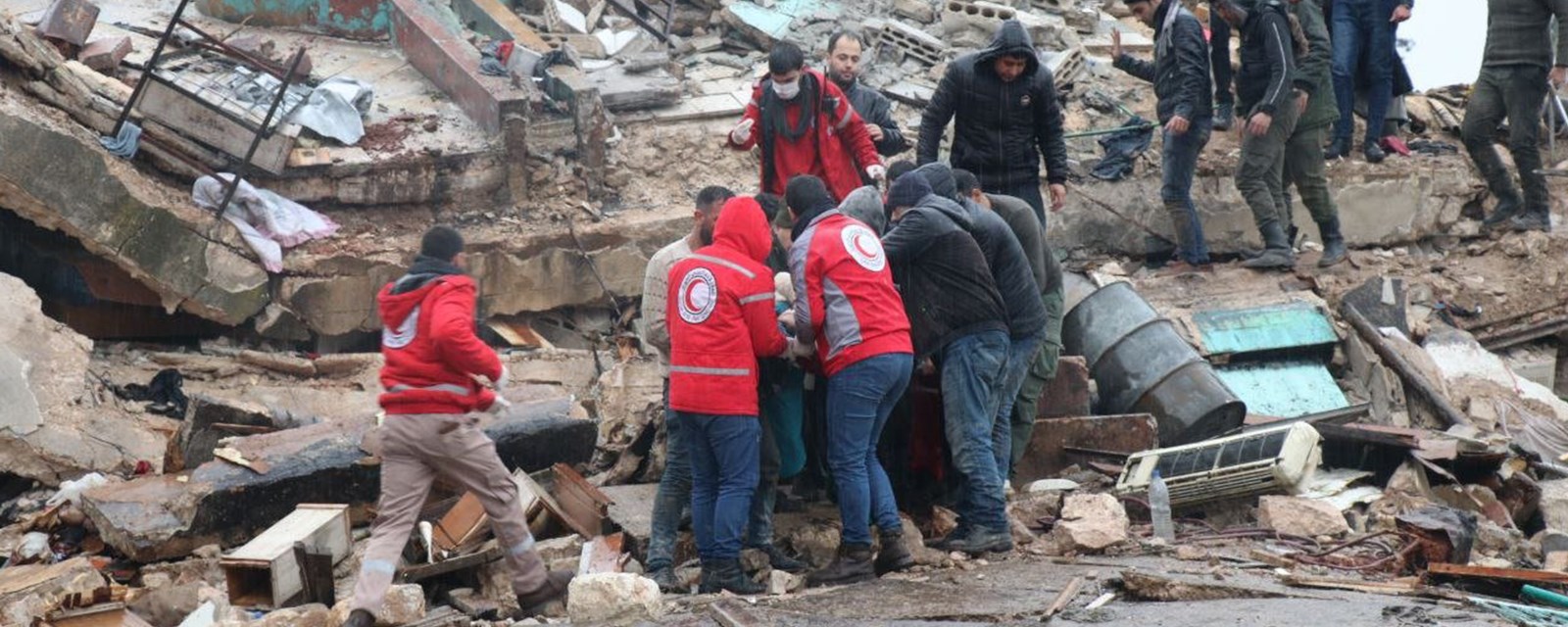Redningsmanskaper fra Syrisk Røde Halvmåne bærer ut et menneske fra en sammenrast bygning.