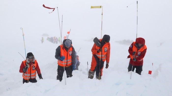 Fire personer fra Hjelpekorpset står ute i snøstorm og stikker lange pinner ned i snøen.