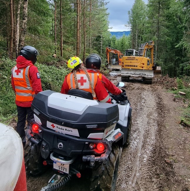 Frivillige fra Røde Kors kjører ATV med tilhenger gjennom en gjørmete skog