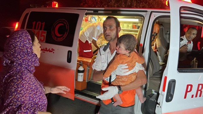 Mannlig ambulansepersonell fra Palestinsk Røde Halvmåne bærer et barn ut av en ambulanse
