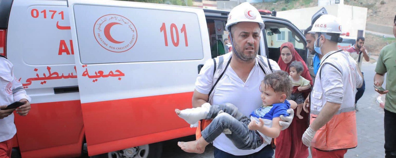 En mann løper ut av en ambulanse med et lite barn i armene.