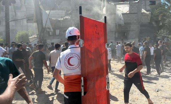 En frivillig fra Palestinsk Røde Halvmåne står foran en ruin med en båre i hånden.