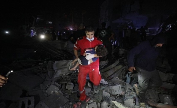 En mann fra Palestinsk Røde Halvmåne bærer et barn ut av ruiner i mørket.