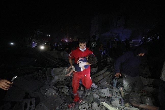 En mann fra Palestinsk Røde Halvmåne bærer et barn ut av ruiner i mørket.