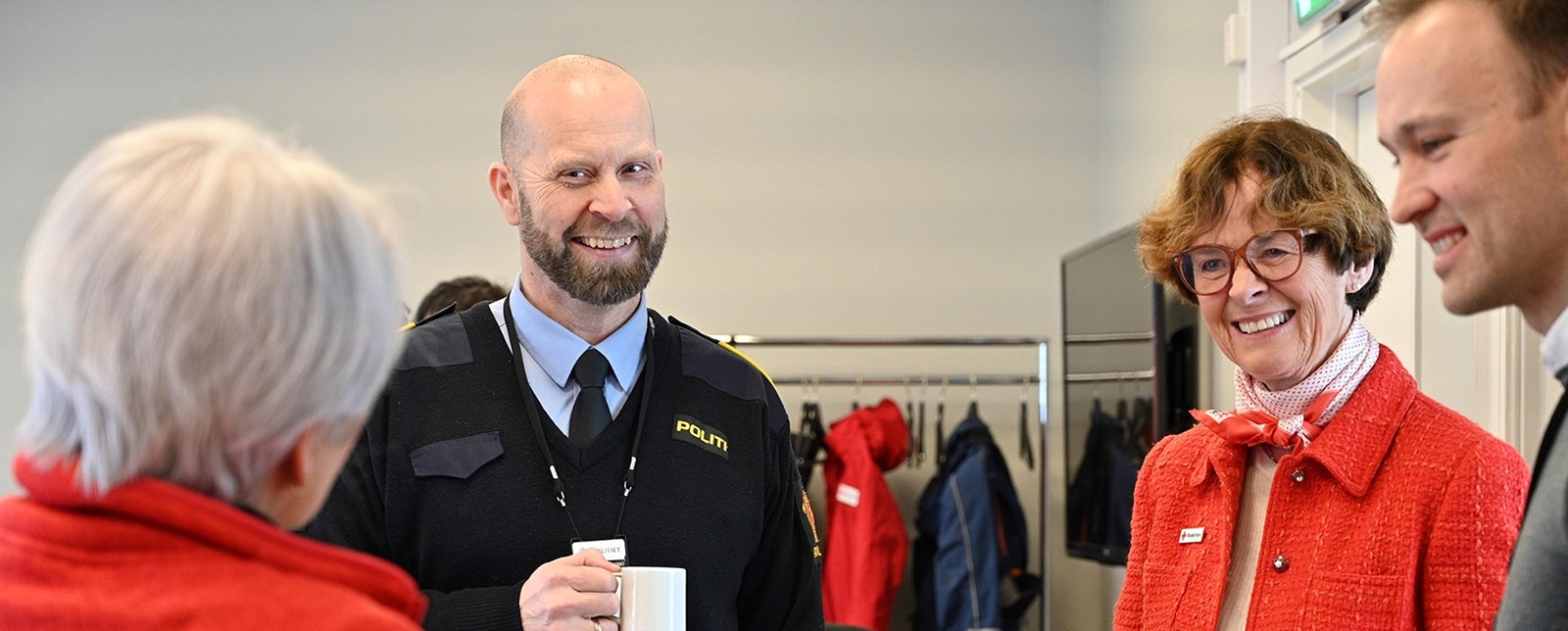 Fire mennesker som smiler, drikker kaffe og prater sammen.