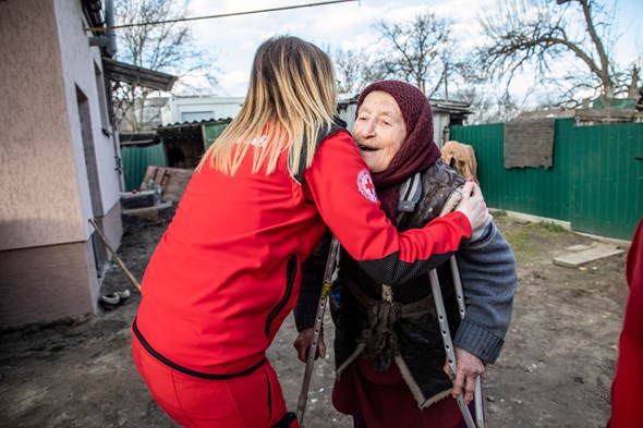 Kvinne i Røde Kors-uniform klemmer en gammel dame