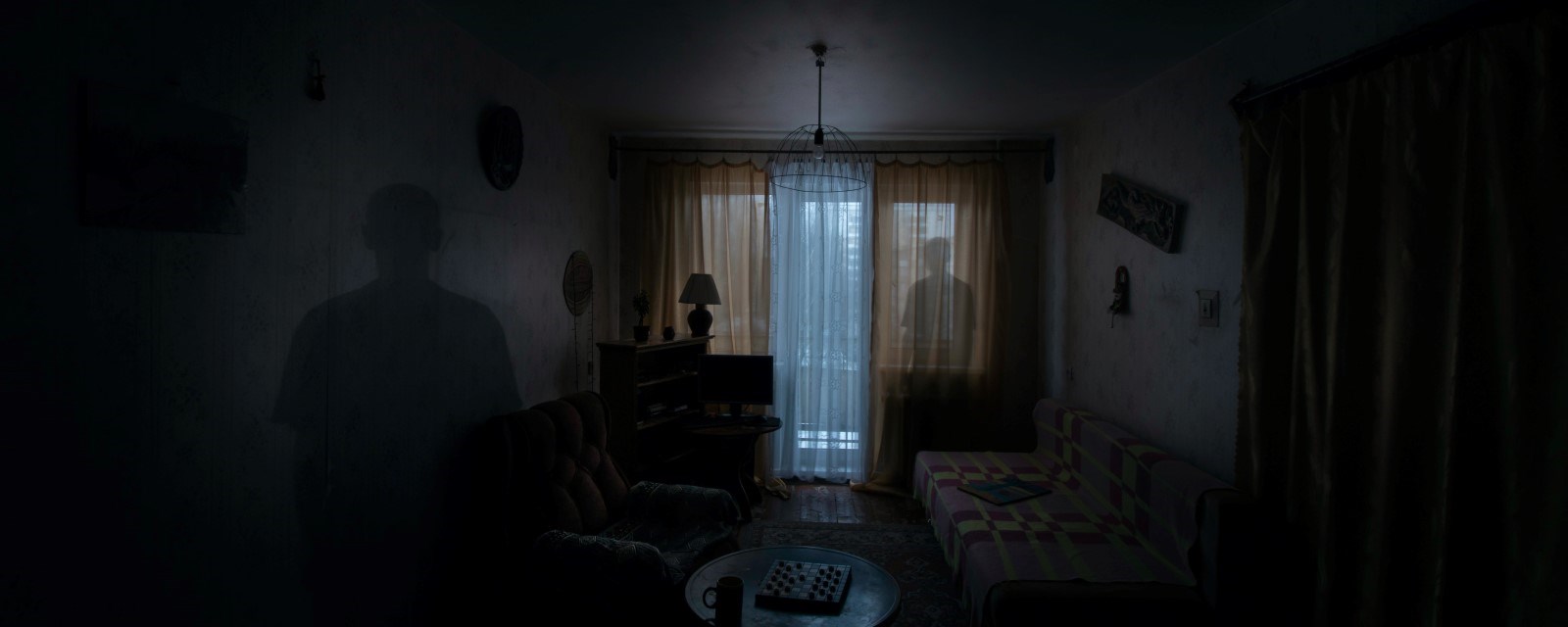 En mørk stue der man ser skyggen av en person i vinduet)