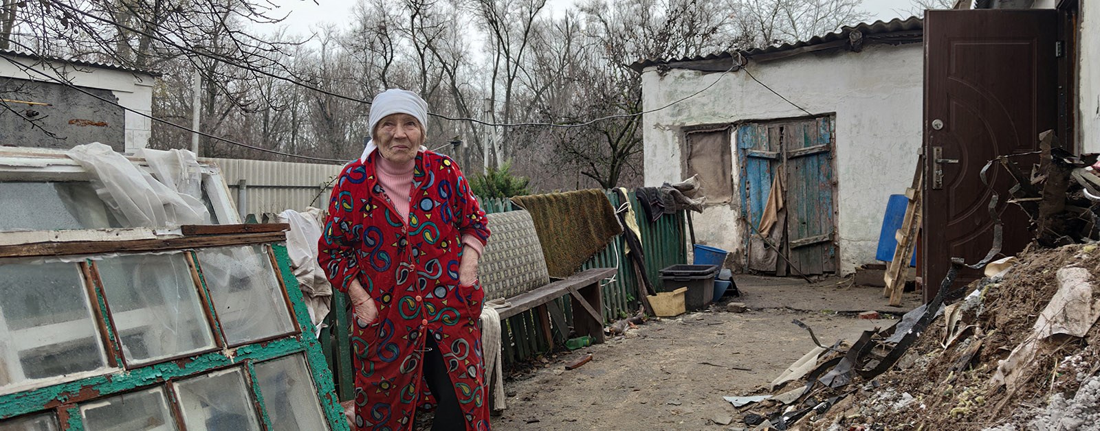En eldre kvinne står foran hjemmet sitt i det østlige Ukraina. 