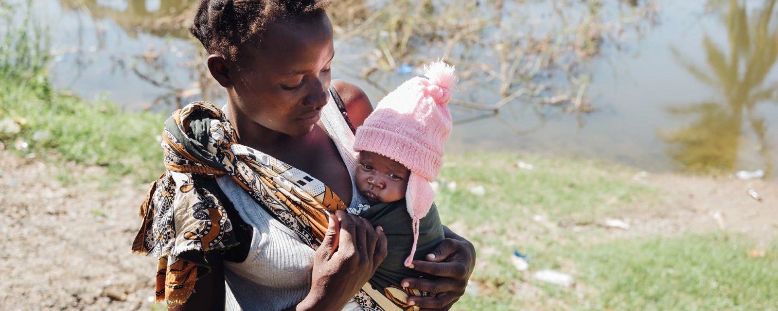 En ung mor med sitt barn på armen står ved vannkanten