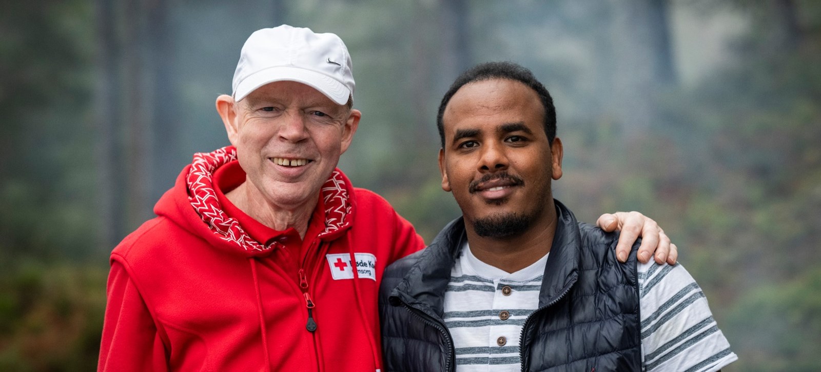 En mann som er frivillig i Røde Kors holder armen sin rundt en annen mann som han er flyktningguide for.