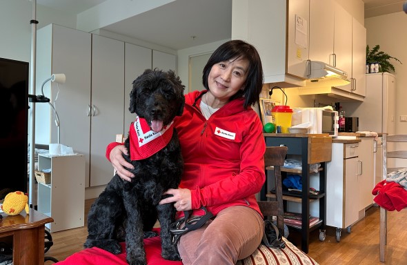 En kvinne med kort svart hår sitter med en svart hund på fanget.