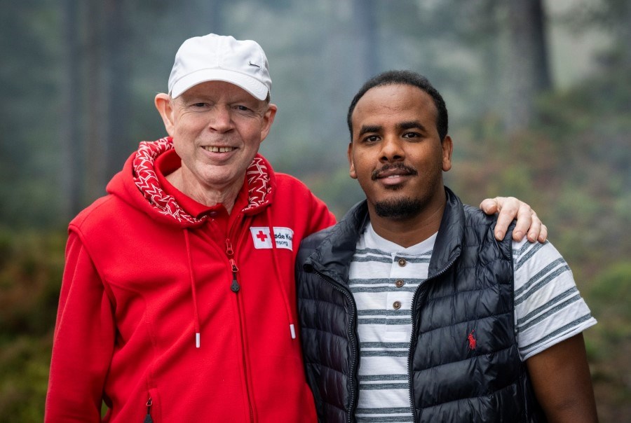 En endre mann som er flyktninggguide i Røde Kors holder armen sin rundt den han besøker.