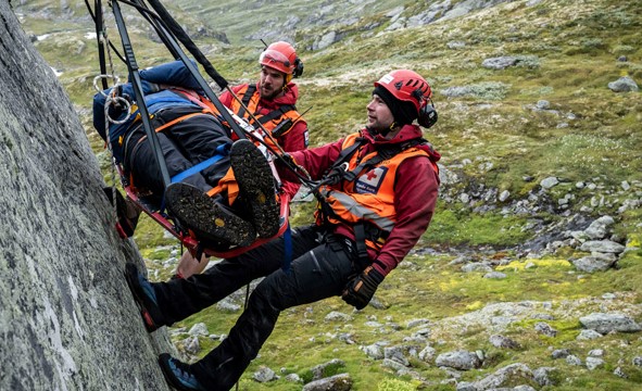 To frivillige fra Røde Kors rappellerer ned et fjell med en skadet person som ligger i en båre.