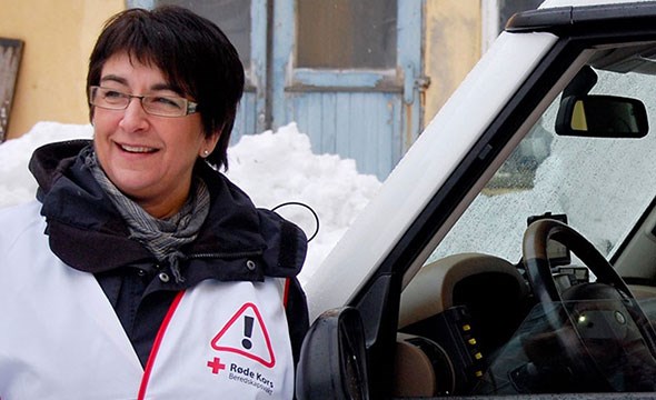 En kvinne med hvit vest merket med beredskapsvakt lener seg inn mot bil, ute, vinter