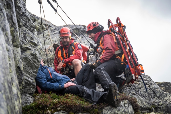 To frivillige fra hjelpekorps hjelper en i fjellet