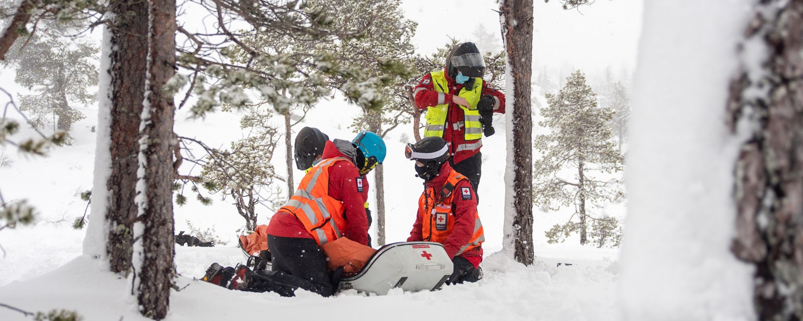 Fire stykker i Røde Kors uniform står over en pulk i snøen