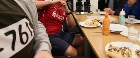 Insatte sitter ved bordet og spiser pizza laget sammen med frivillige i Røde Kors