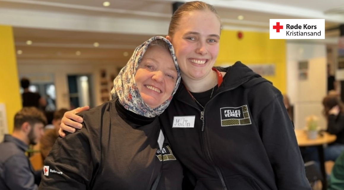 En gruppe Røde Kors-frivillige står samlet ute i et snødekt fjellområde, alle iført røde jakker og oransje refleksvester. De smiler mot kameraet i solskinnet, og en liten hund i sele står foran gruppen. I bakgrunnen ses skiutstyr og en person med lue som ser mot gruppen.