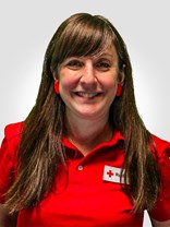 Portrettbilde av ei kvinne med langt brunt hår, to røde øredobber, et smått smil, med røde kors uniform på.