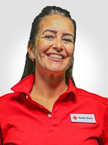 Portrettbilde av ei kvinne med langt mørk brunt hår, øredobber og et stort smil, med røde kors uniform på.