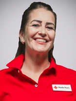 Portrettbilde av ei kvinne med langt mørk brunt hår, øredobber og et stort smil, med røde kors uniform på.