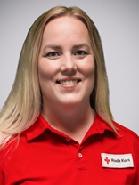 Portrettbilde av ei ung kvinner med langt blondt hår og stort smil, med røde kors uniformen på.