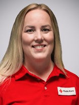 Portrettbilde av ei ung kvinner med langt blondt hår og stort smil, med røde kors uniformen på.