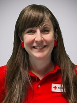 Portrettbilde av ei kvinne med langt brunt hår, to røde øredobber, et smått smil, med røde kors uniform på.