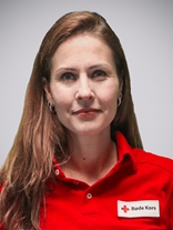 Portrettbilde av ei kvinne med langt brunt hår, to røde øredobber, et smått smil, med røde kors uniform på.