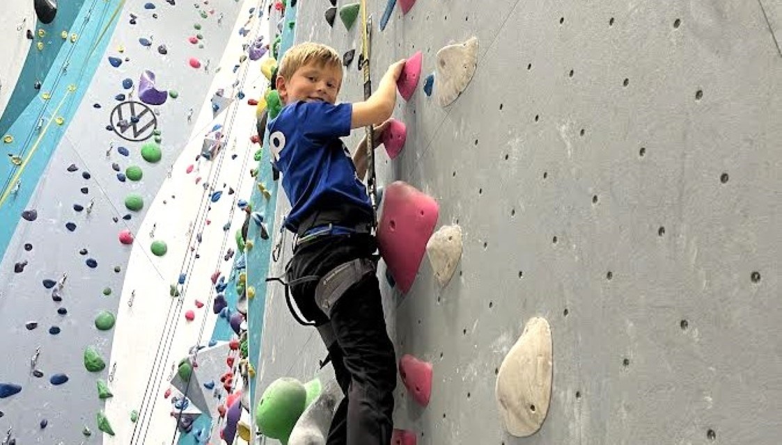 Gutt fra Røde Kors Familiesenter klatrer opp klatrevegg under aktivitetstur i Kristiansand. Fokus og mestring i trygge omgivelser.