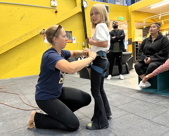 Frivillig hjelper jente med å feste klatreselen under aktivitet med Røde Kors Familiesenter. Trygghet og lek i fokus.