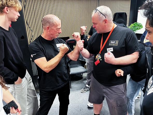 To voksne menn som later som om de er i fysisk konflikt foran en del ungdommer.