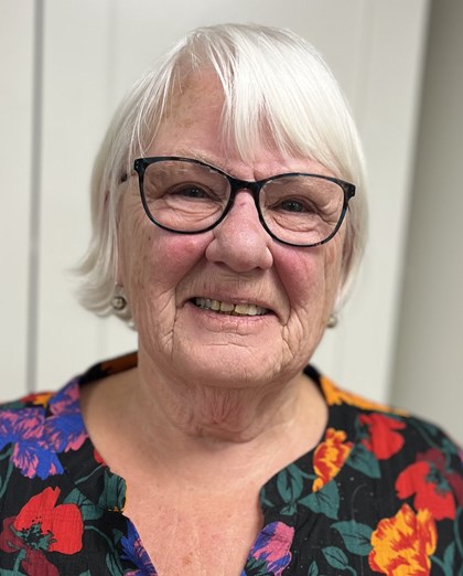 Portrettbilde av en eldre dame med briller og hvit hår, har på seg en bluse.