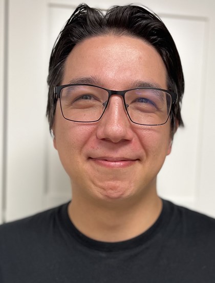 Portrettbilde av en ung mann med kort hår og tynne briller, har også en skjorte.