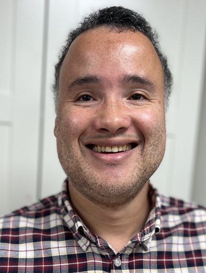 Portrettbilde av en ung mann, nylig barbert og stort bredt smill. Kort hår, og rutete skjorte.