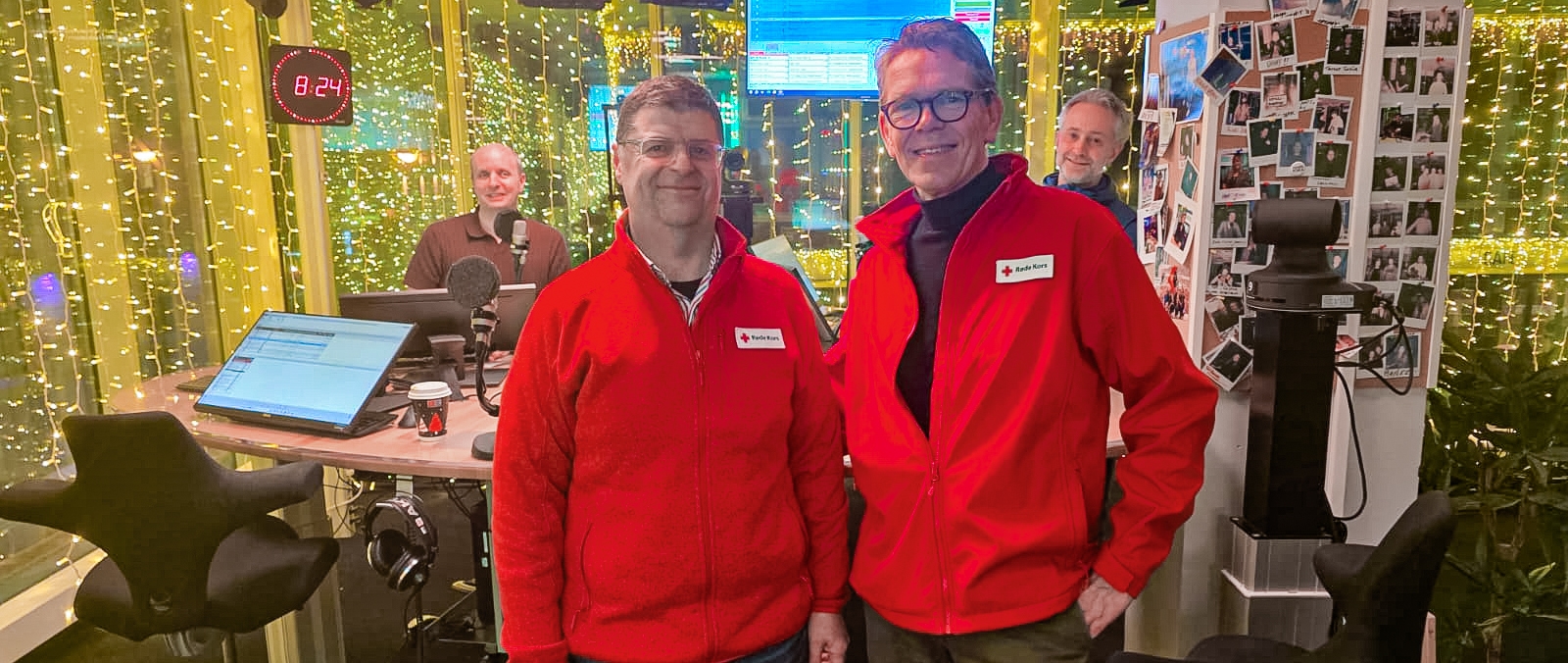 Fire personer står i et radiostudio pyntet med lyslenker. Foran står Yngve Stiansen og Håvard Raustøl, begge i røde Røde Kors-jakker. Bak dem står Alfred Solgaard og Rabih Costantine ved studiopulten med mikrofoner og skjermer. Stemningen er uformell og vennlig.