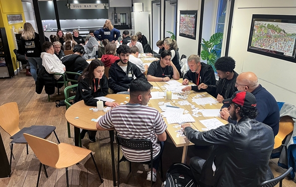 To personer går mot sykehuset på Røde Kors, med parkeringsplasser og moderne bygning i bakgrunnen. Godt vær og avslappet atmosfære.