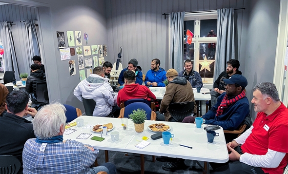 To personer går mot sykehuset på Røde Kors, med parkeringsplasser og moderne bygning i bakgrunnen. Godt vær og avslappet atmosfære.