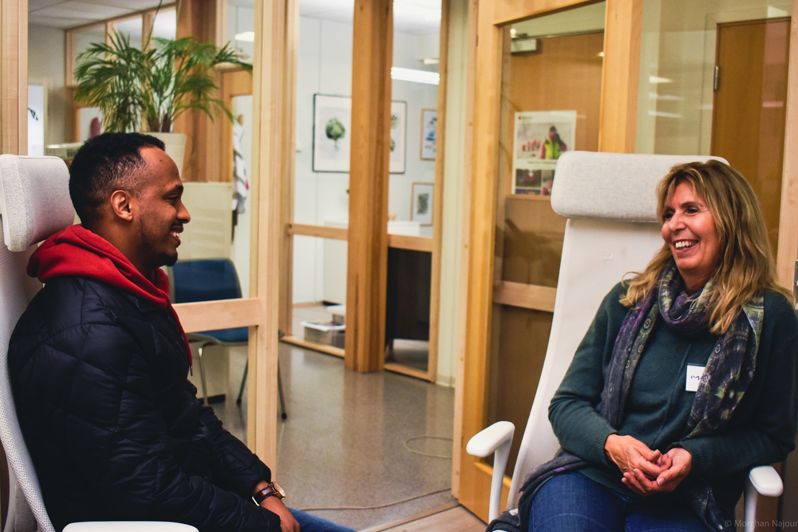 Deltaker og frivillig sitter i hver sin stol og smiler til hverandre