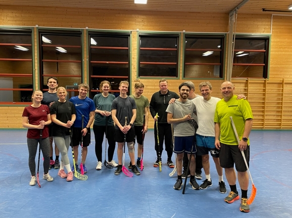 Tolv personer ikledd sporttøy holder innebandy-køller i en gymsal