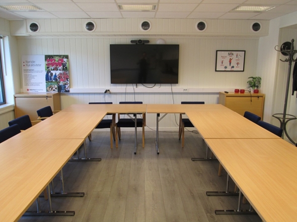 Et rom med bord i hestesko-formasjon og en TV som henger på veggen