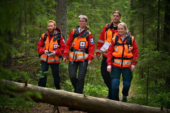 Fire personer i hjelpekorps-uniform går gjennom skogen