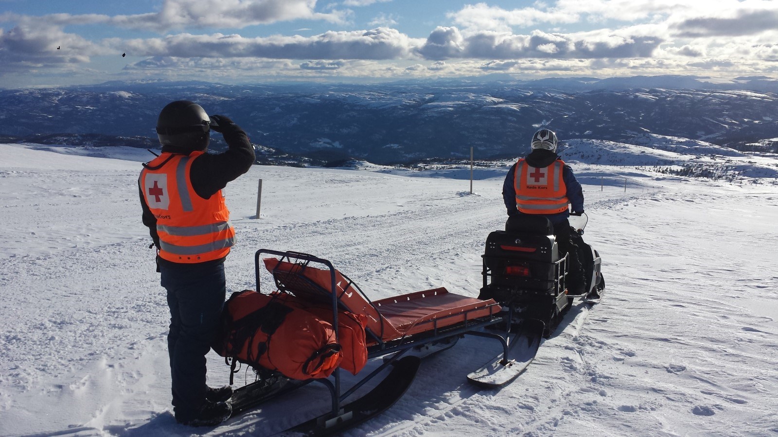 To menn far hjelpekorpsett på scooter med hvitkledd fjelllandskap i bakgrunn